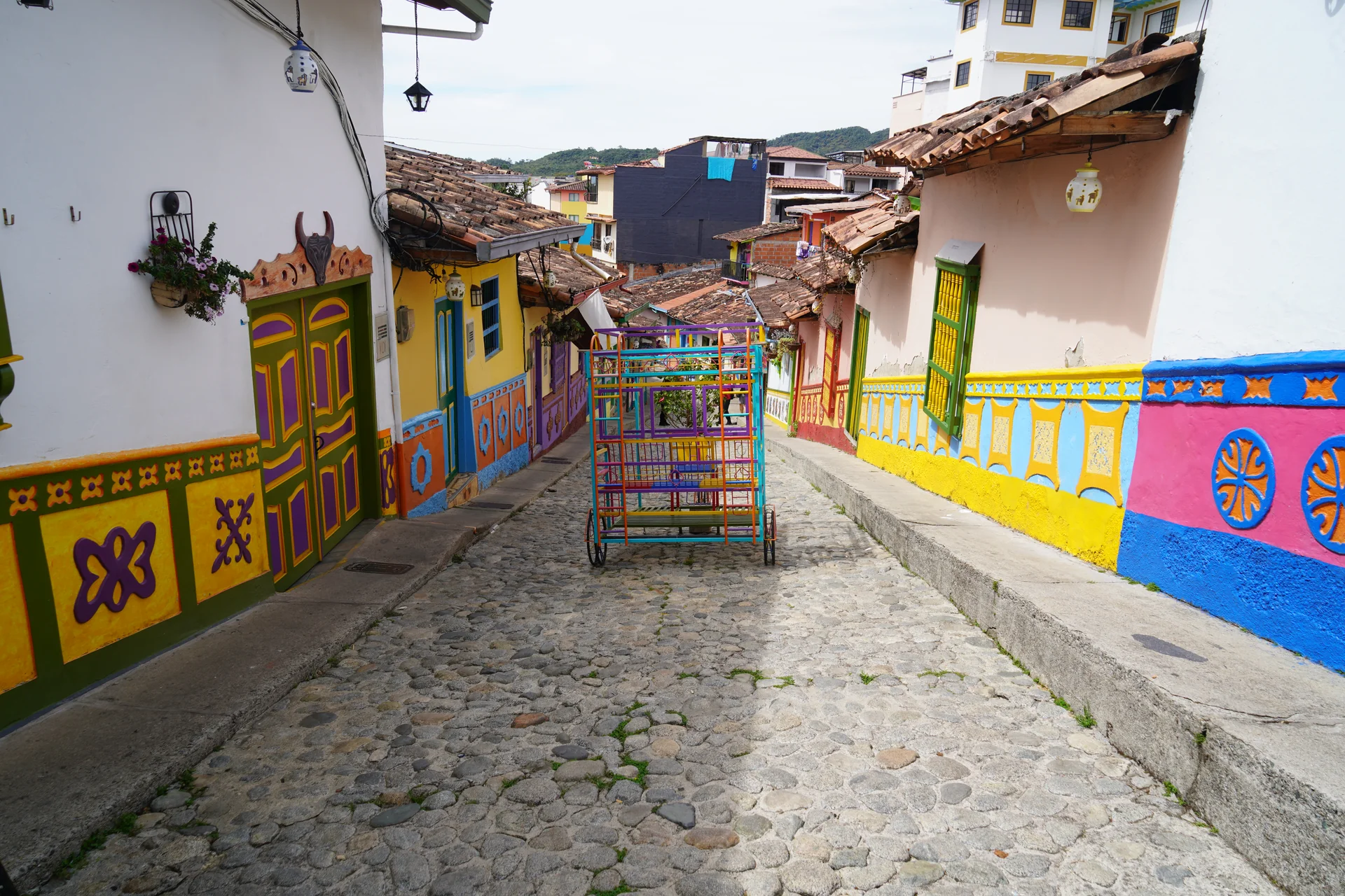 Cobblestone street with flower-filled balconies and zócalo-painted houses, Guatapé