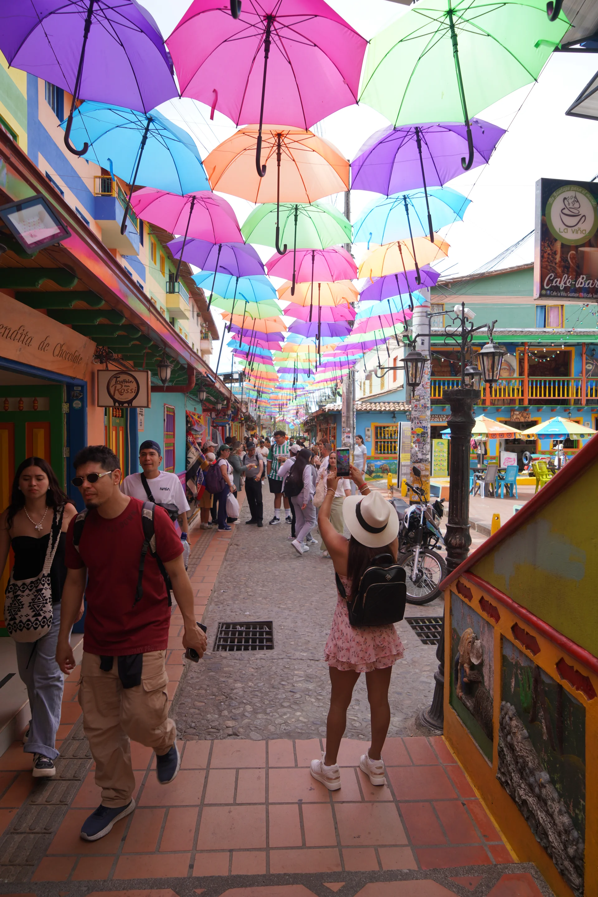 Tourists under the umbrella canopy with zócalo buildings on both sides, Guatapé