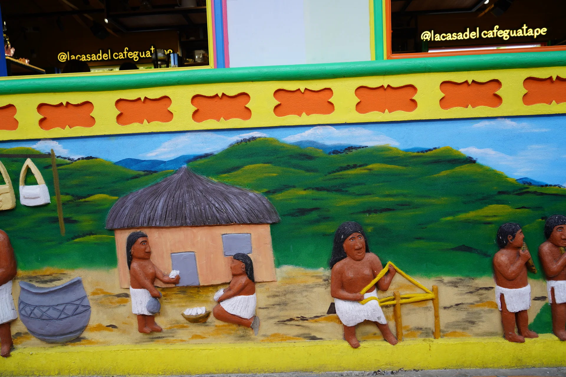 Tahamí village community scene in hand-sculpted zócalo art, Guatapé